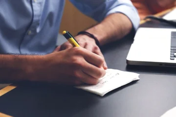 Homem escrevendo em um bloco de notas questões do concurso PGM RJ.