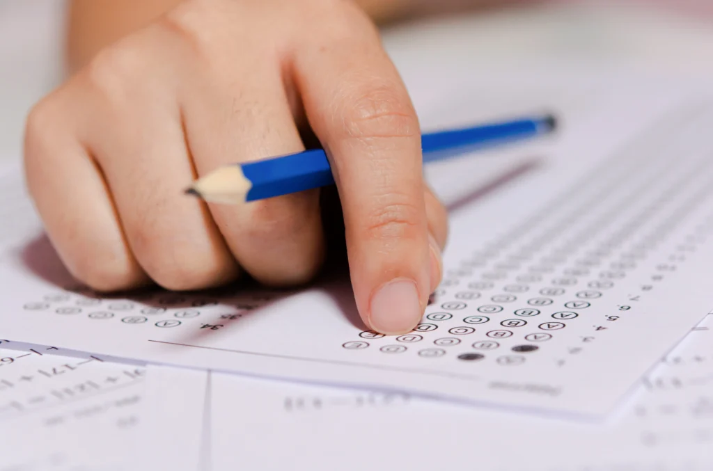 Mão de estudante segurando lápis e folhas de respostas