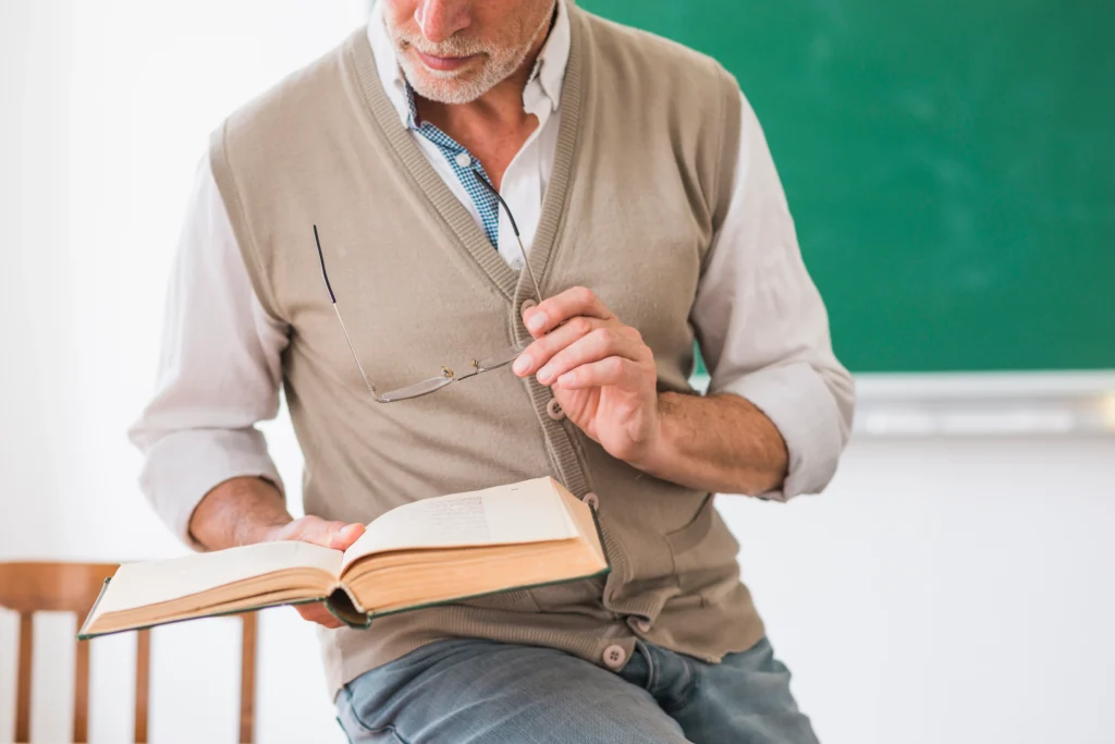 Professor segurando o livro e óculos em sala de aula